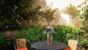 A round metal table with two wicker chairs, each with an orange cushion, and a vase with flowers in the center. - a'Vue Guesthouse (Cape Town)