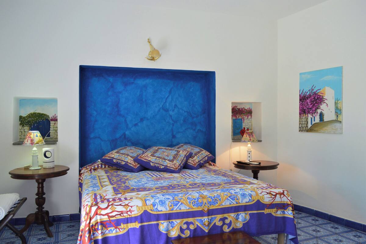 A bedroom with a large bed, a round wooden table, and a nightstand with a lamp.