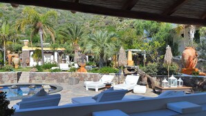 A poolside area with lounge chairs, a stone wall, and a view of a mountainous landscape. - Hotel Oasi (Lipari)