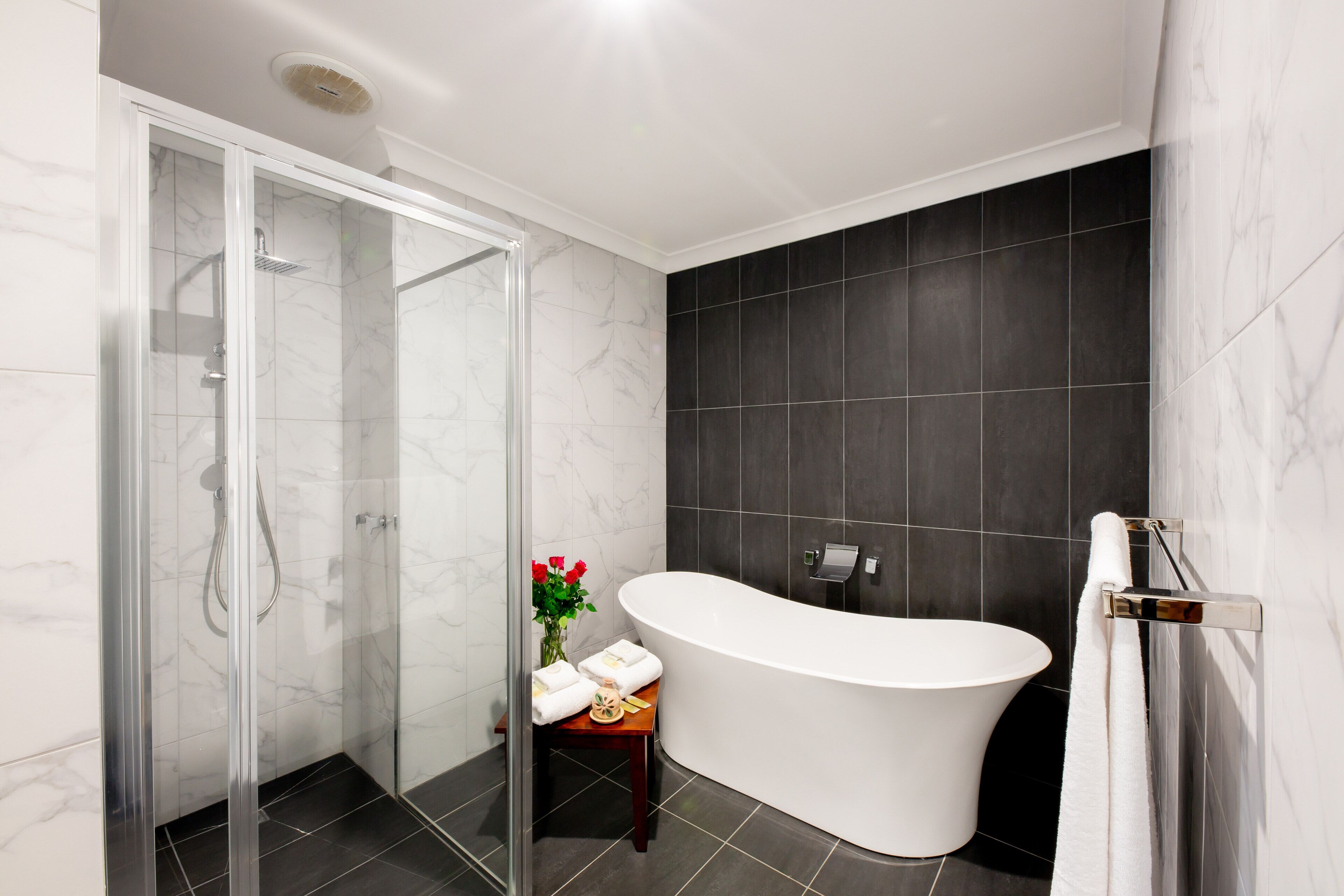 Une salle de bain moderne dotée d’une douche à parois de verre, d’une baignoire sur pieds et de murs recouverts de carreaux foncés.