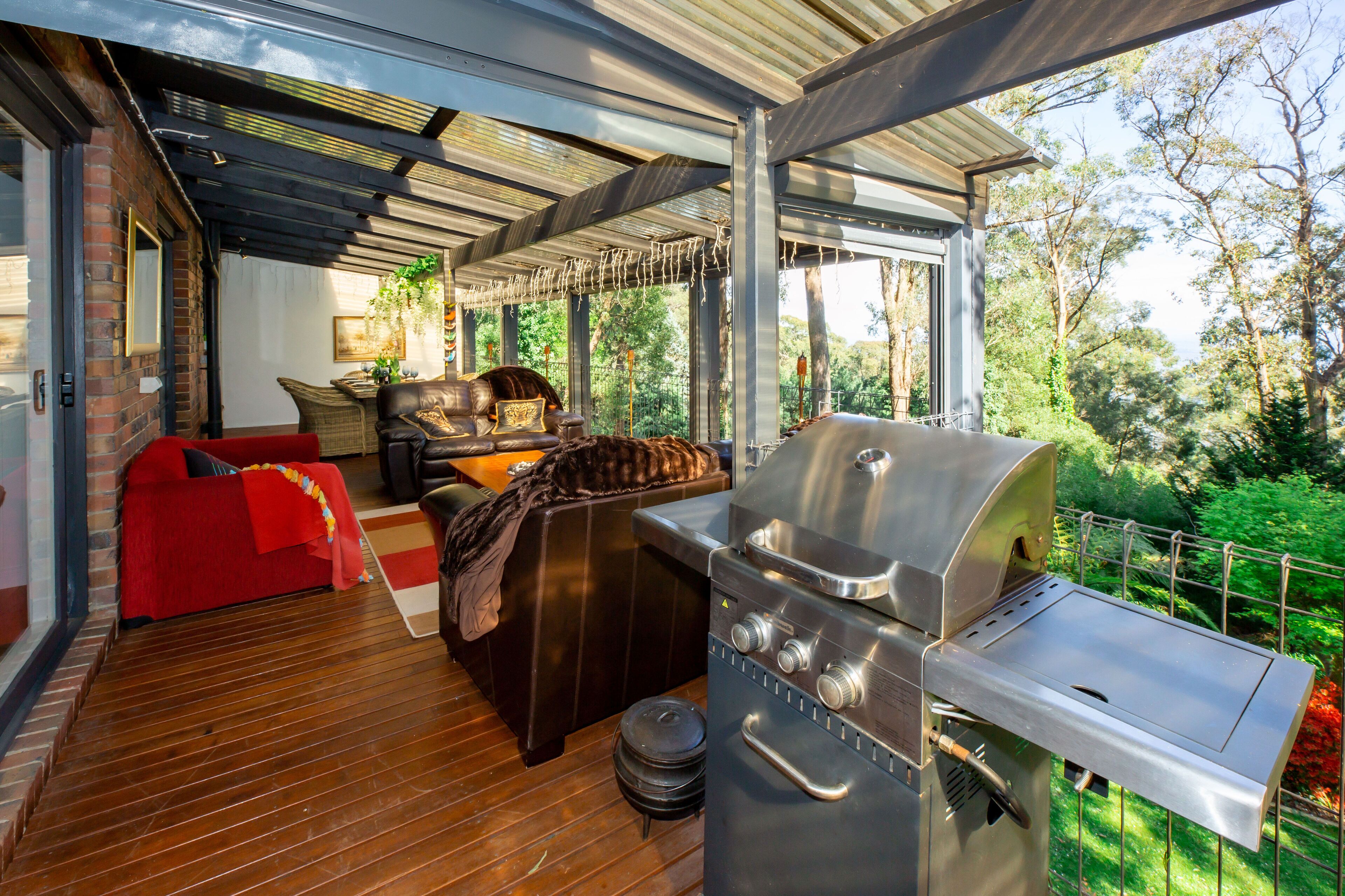 A covered outdoor area with a grill, a red sofa, and a wooden deck.