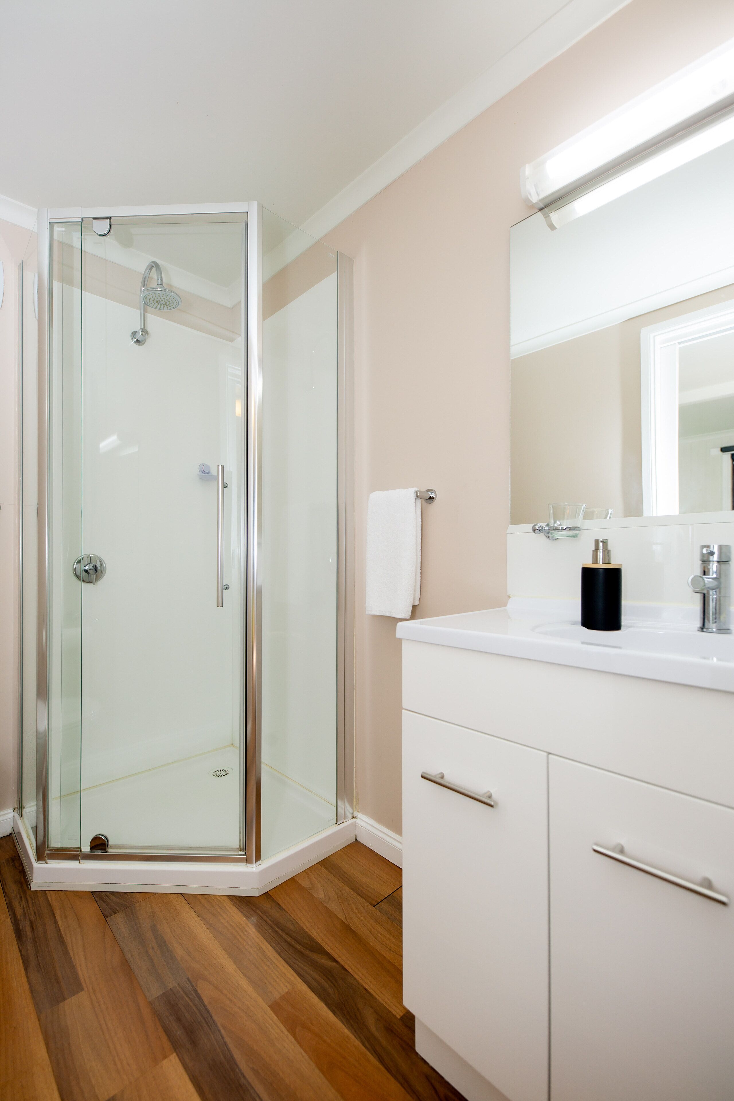 A modern bathroom with a glass shower enclosure, a white vanity with drawers, and a mirror above the sink.