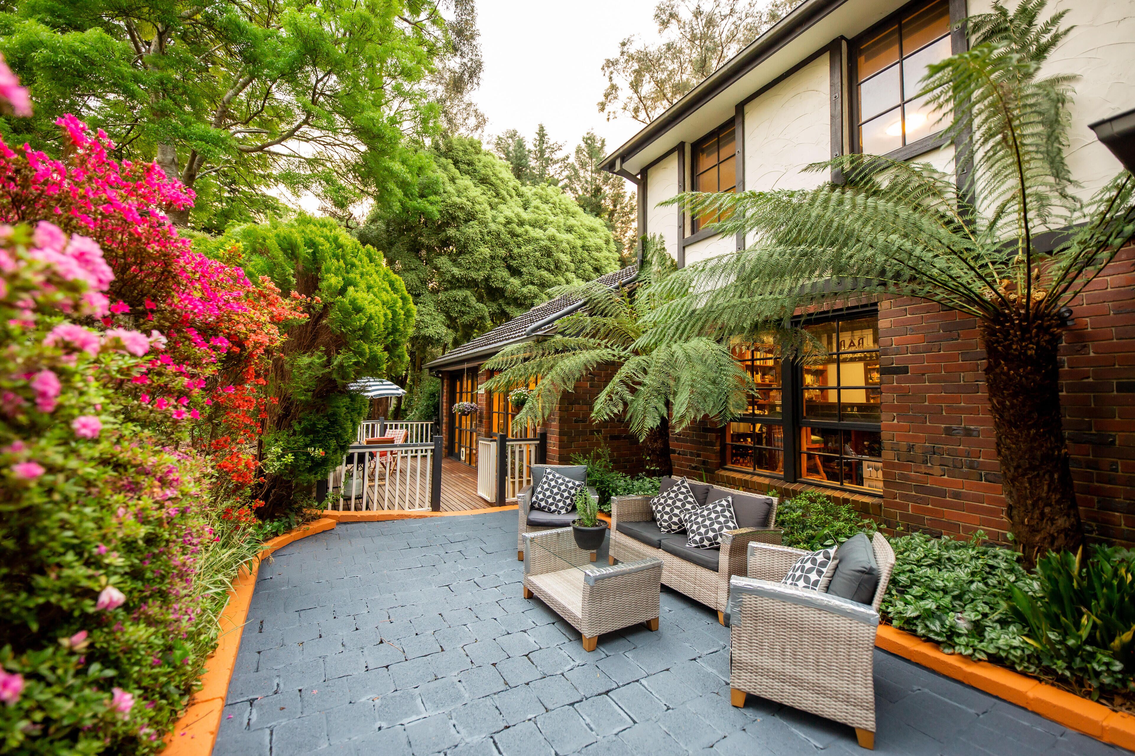 An outdoor patio with wicker furniture, a brick building, and lush greenery.