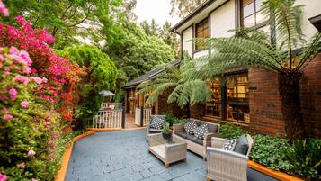 An outdoor patio with wicker furniture, a brick building, and lush greenery.
