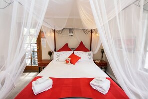 Ein Bett mit roter Bettdecke, weißen Kissen und einem Baldachin.