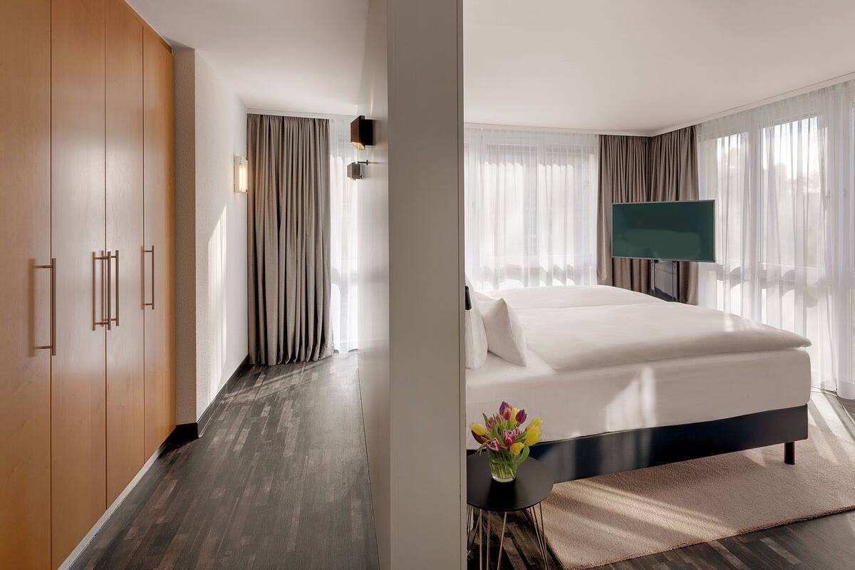 A modern hotel room with a large bed, a flat-screen TV, and a view of the outdoors.