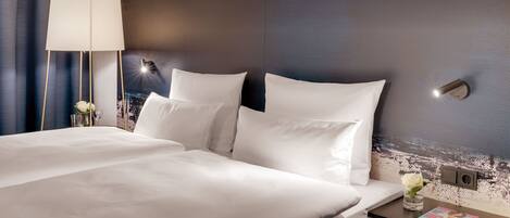 Una habitación de hotel con una cama grande, una mesita de noche con lámpara y una revista sobre la mesa.