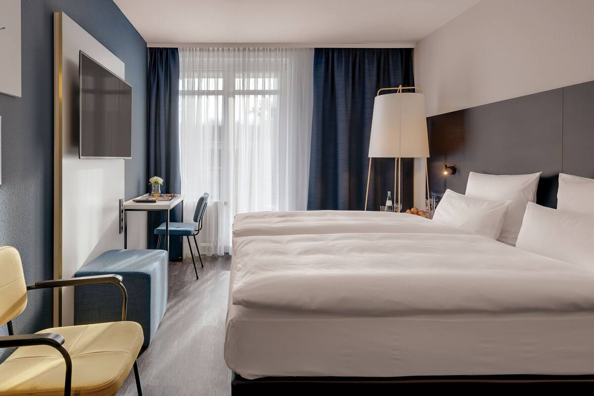 A hotel room with a bed, a desk, a chair, a TV, and a window with curtains.