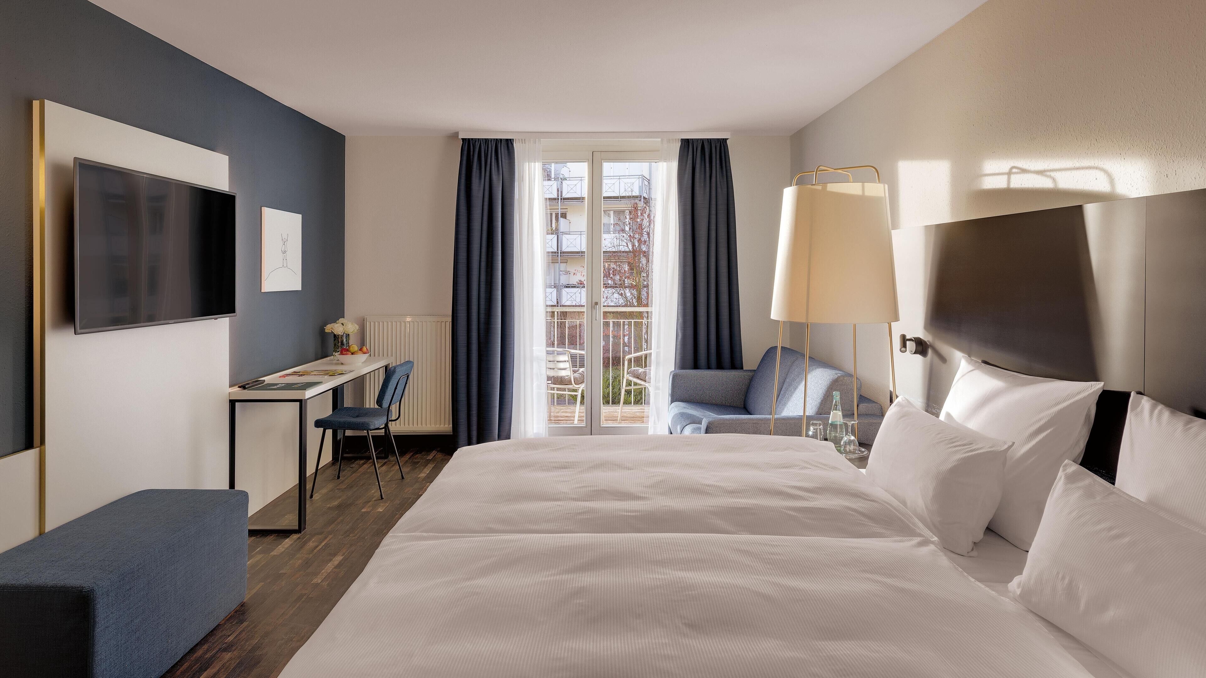 Een hotelkamer met een groot bed, een bureau met stoel, een televisie en uitzicht op het balkon.