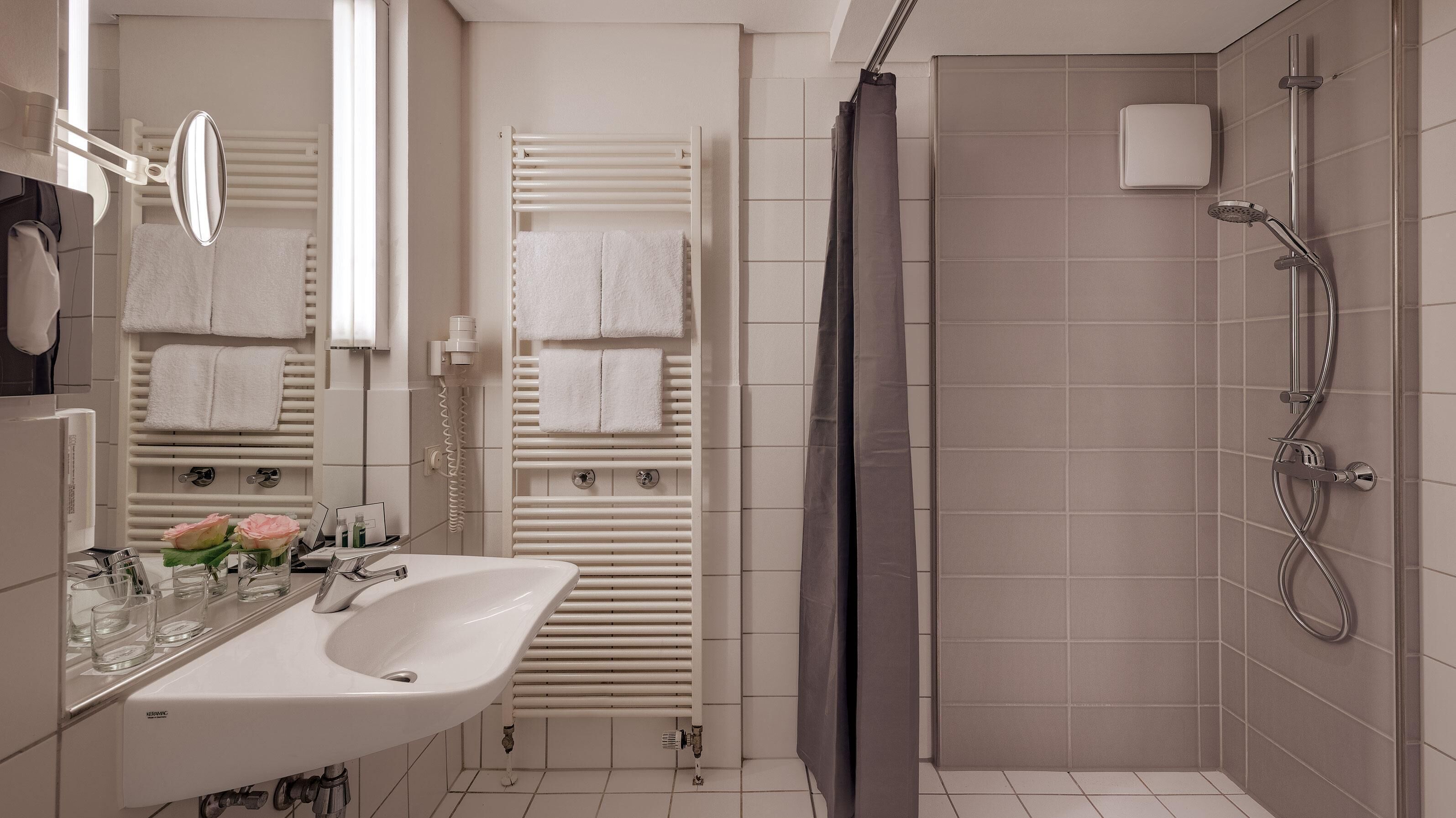 Un baño moderno con lavamanos, espejo y toalleros blancos.
