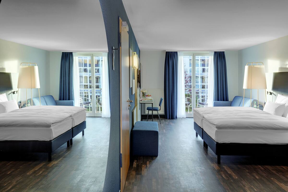 A hotel room with two beds, a desk, and a view of the outdoors.