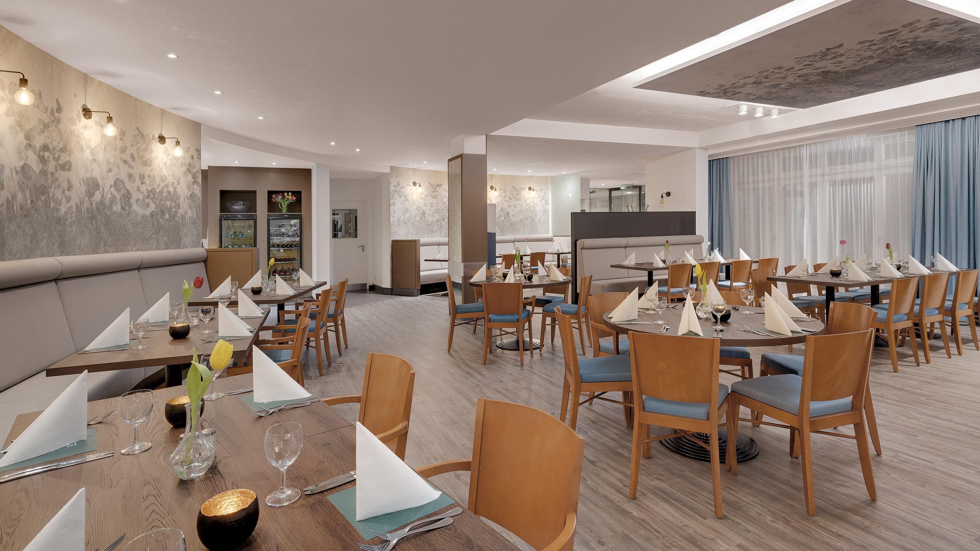 Un comedor de hotel con varias mesas redondas, sillas de madera y un diseño interior moderno.