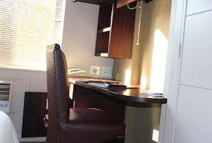 A compact kitchen with a wooden counter, a chair, and a window with blinds. - Illovo Hotel (Sandton)