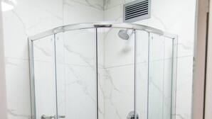 A glass-enclosed shower with a white marble wall and floor, a white towel on the floor, and a black shelf with a white towel. - Illovo Hotel (Sandton)