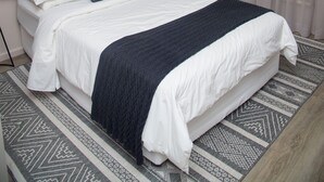 A neatly made bed with a headboard, a bedside table, and a chair. - Illovo Hotel (Sandton)