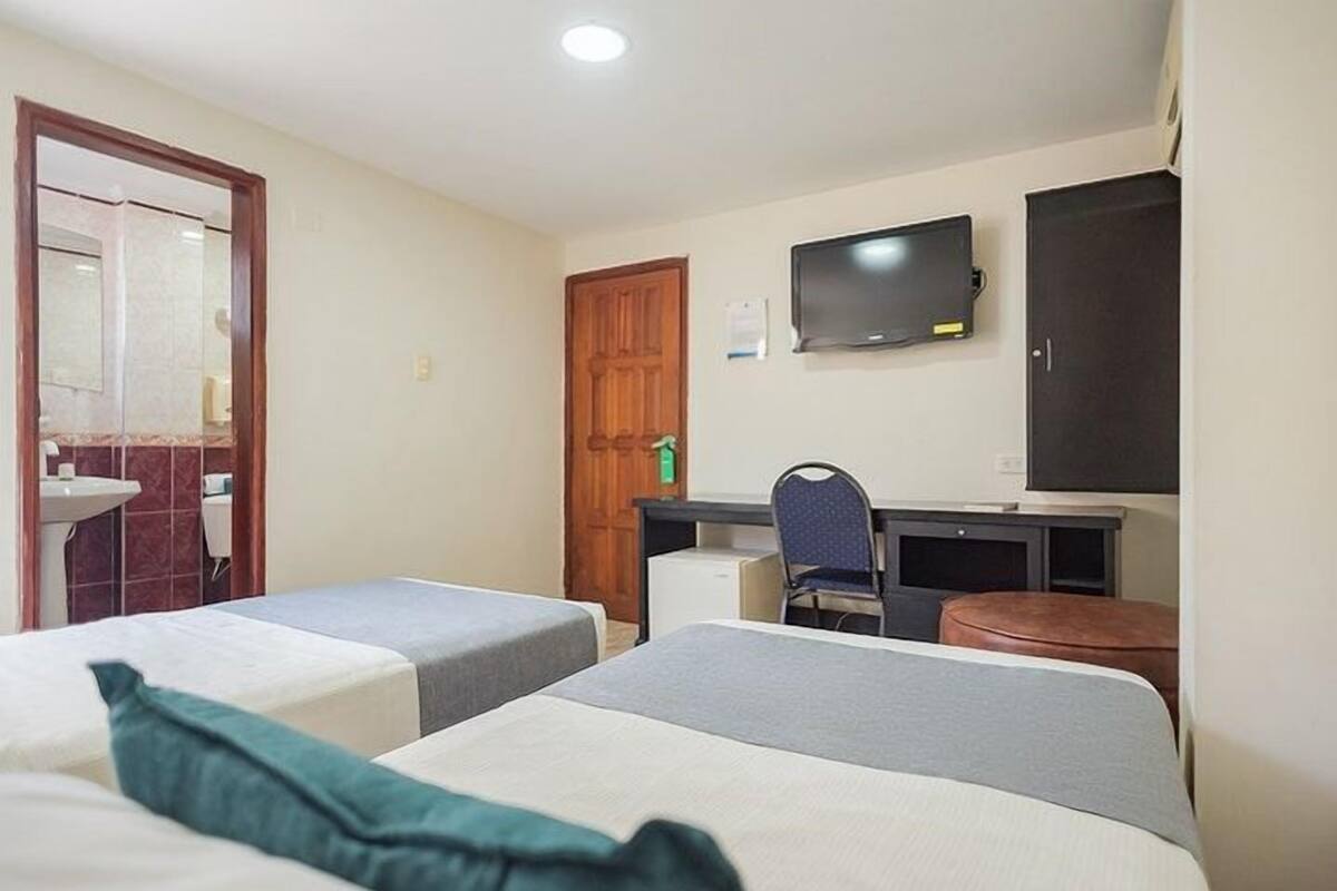 A hotel room with two single beds, a desk with a chair, a television, and a wardrobe.
