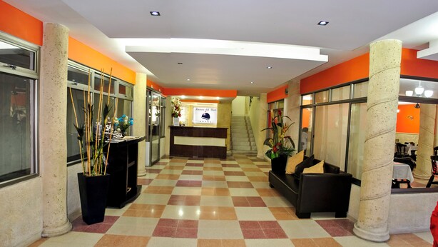 A hotel lobby with a checkered floor, a reception desk, and a staircase leading to the upper floor.