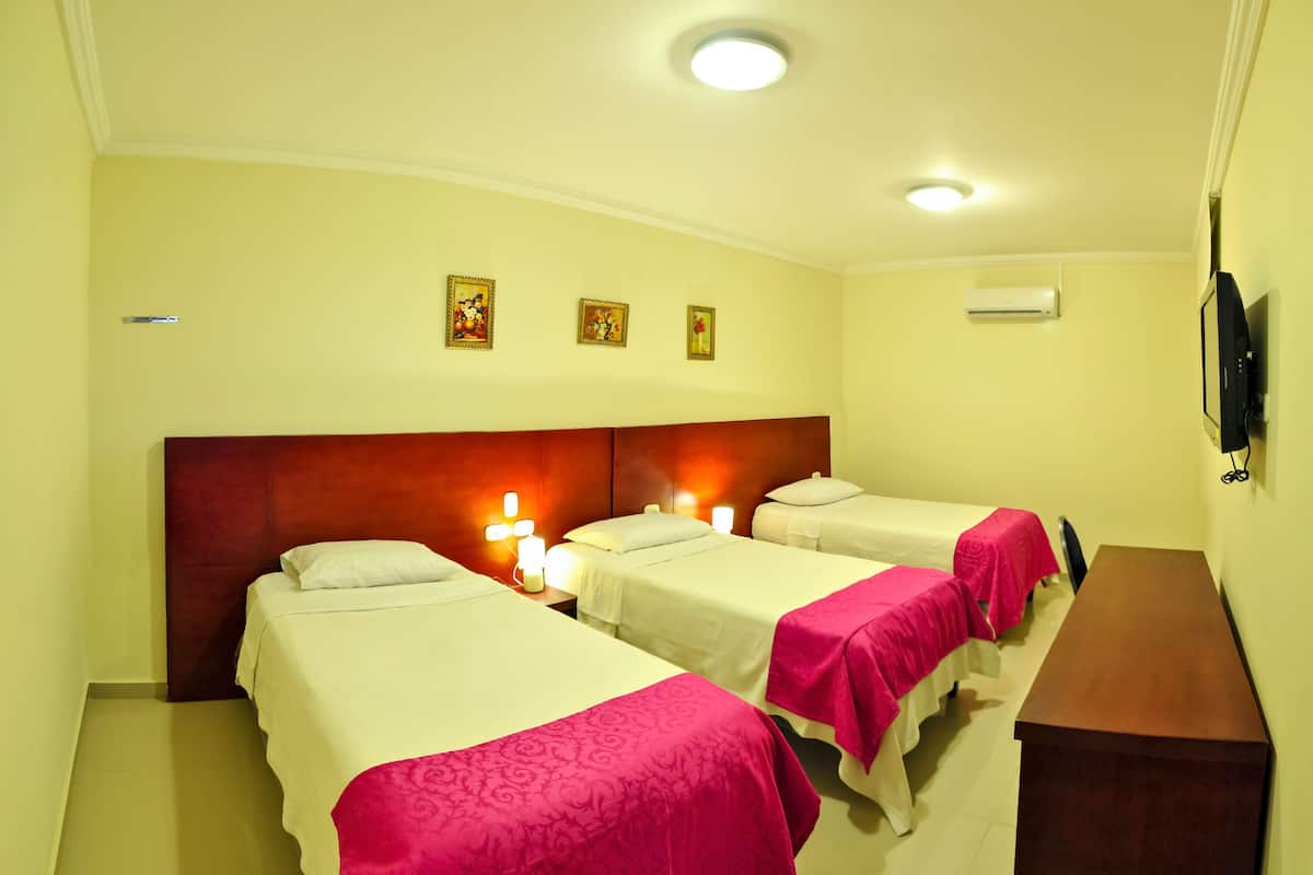A hotel room with three beds, a wooden headboard, a bedside table, and a flat-screen TV mounted on the wall.