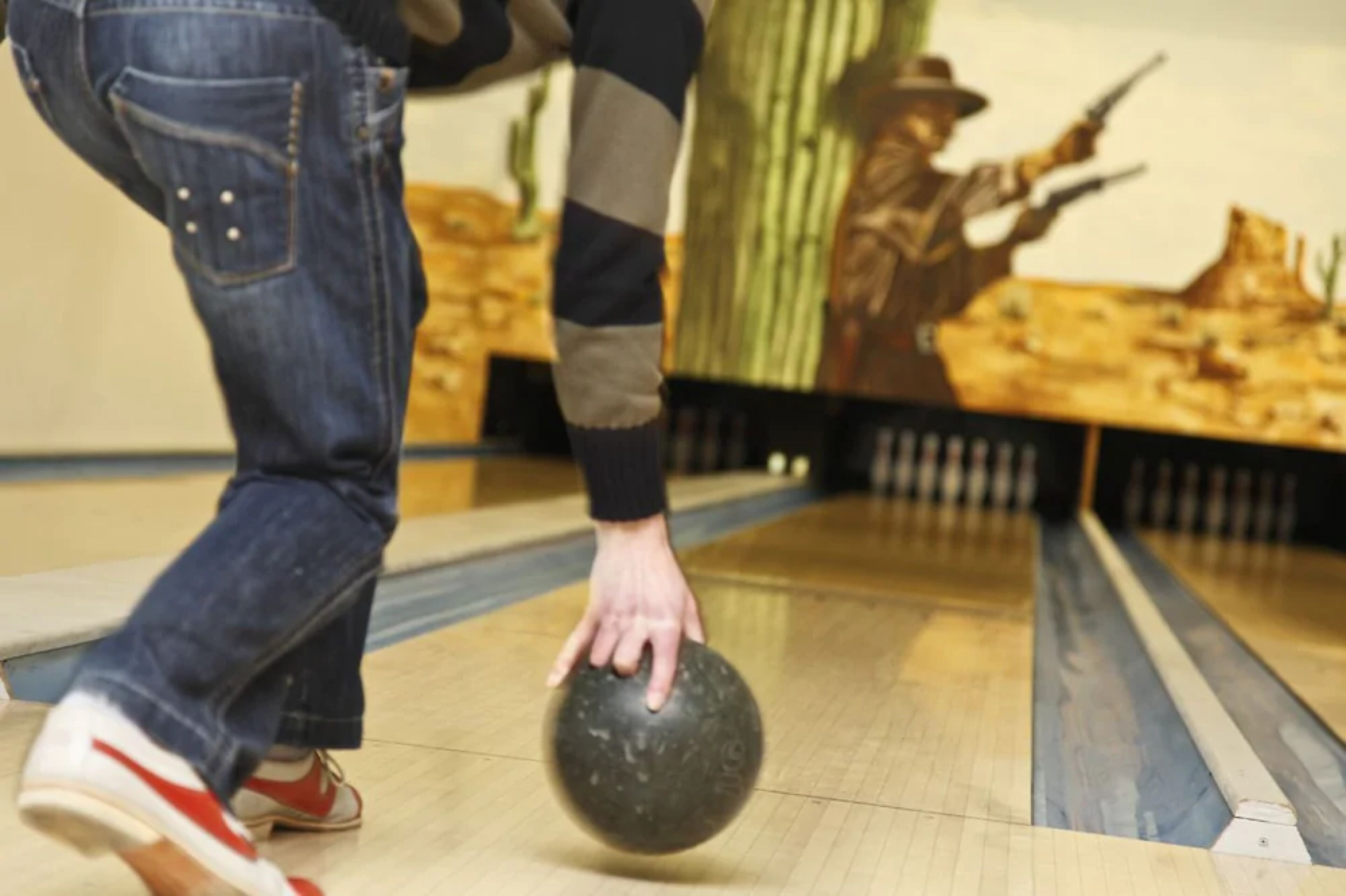 A person bowling with a black ball, wearing jeans and red shoes.
