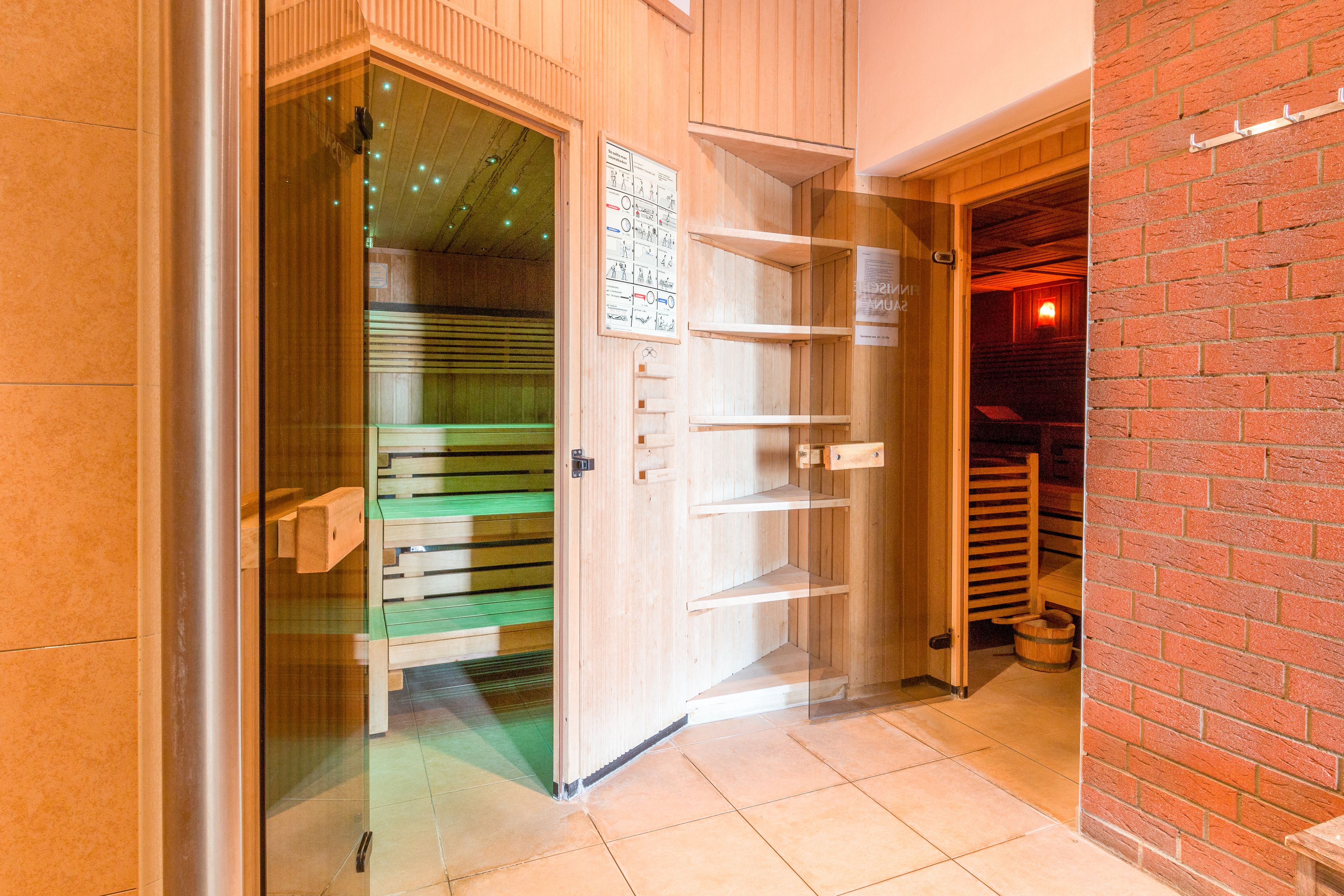 A wooden interior with a glass door leading to a sauna area, a brick wall, and a tiled floor.