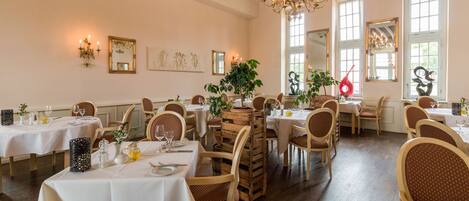 A dining area with multiple tables set for guests, wooden chairs, and a chandelier.