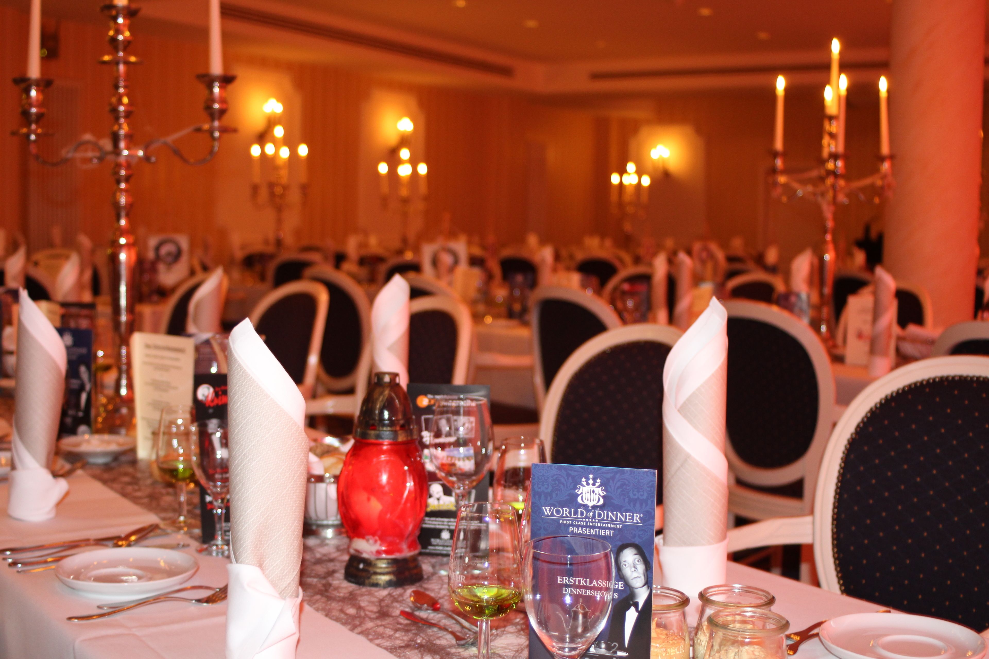A banquet hall with tables set for a formal dinner, featuring chandeliers, candelabras, and a menu stand.