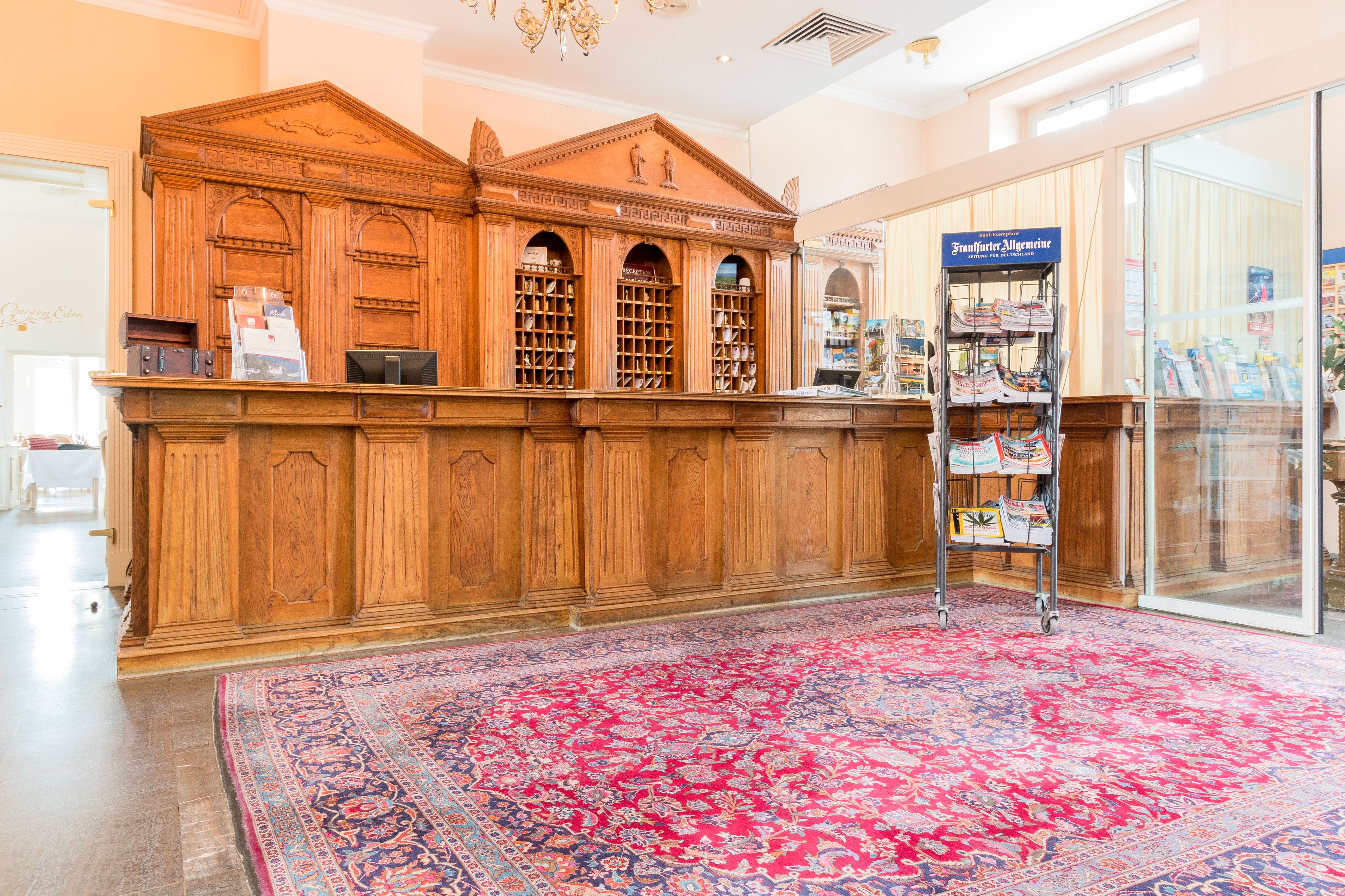 A reception area with a wooden counter, a red patterned carpet, and a glass door leading outside.
