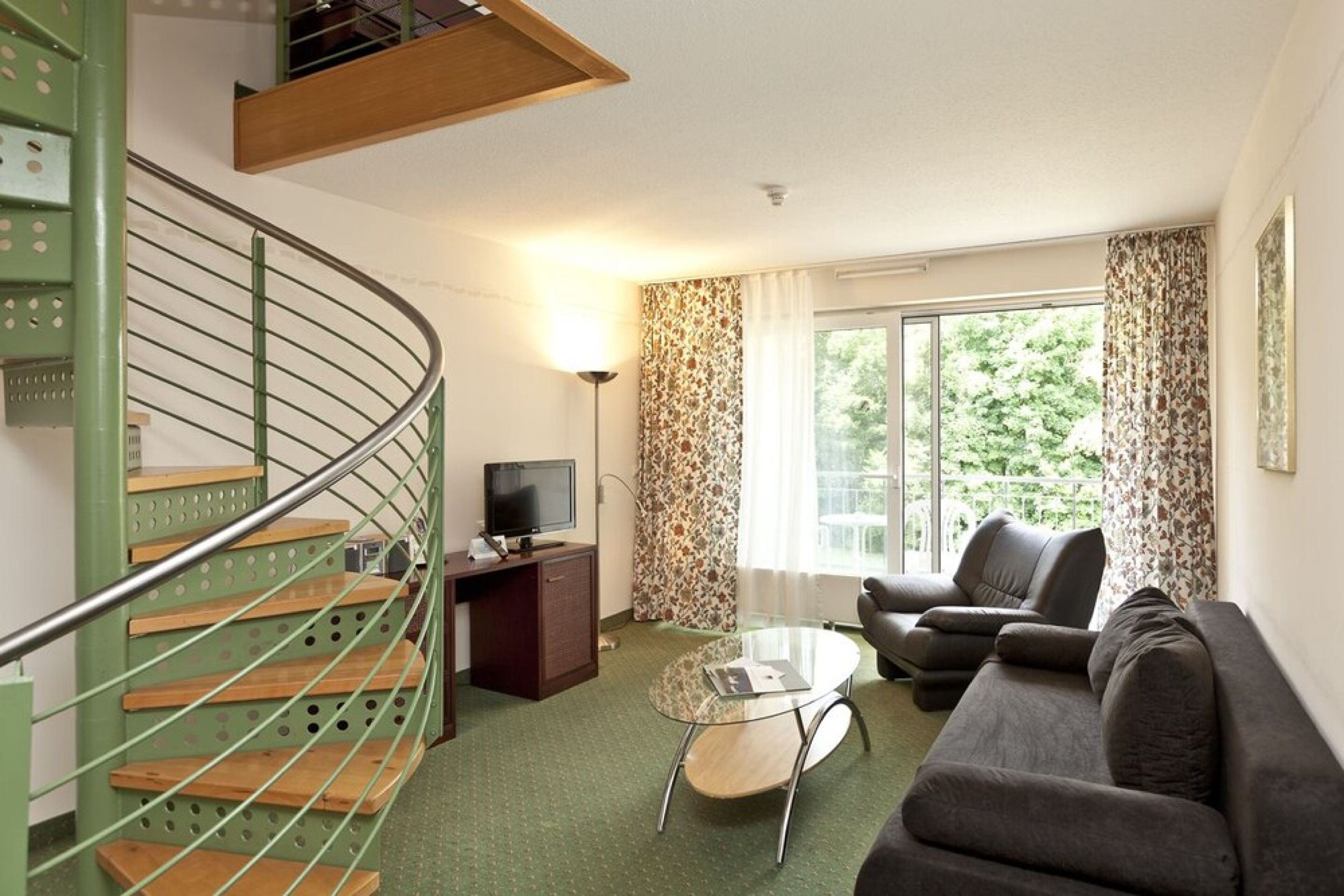 A living room with a green spiral staircase, a sofa, a glass coffee table, and a television.