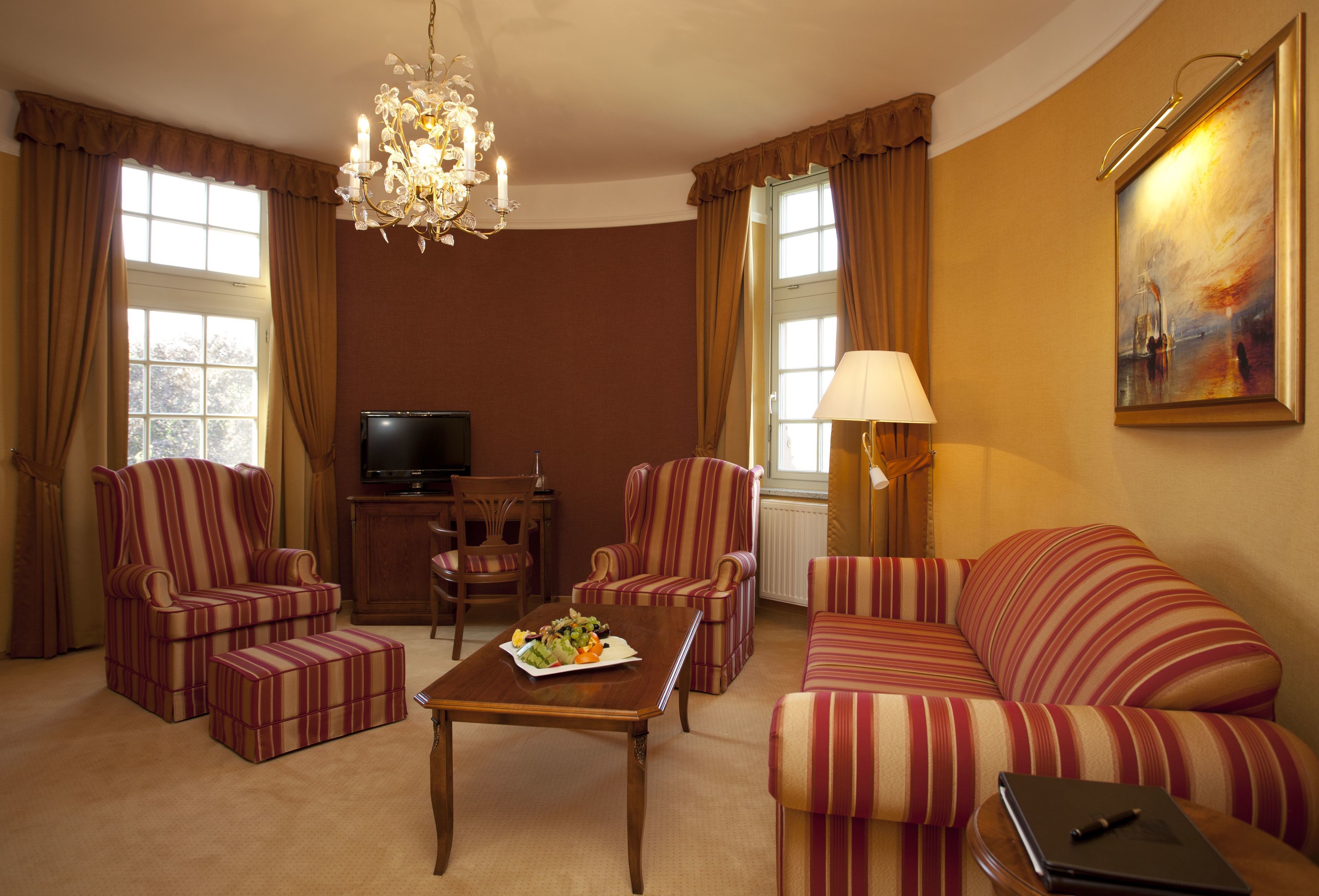 Une chambre d’hôtel avec un canapé, deux fauteuils, une table basse, un téléviseur, une lampe et un tableau au mur.