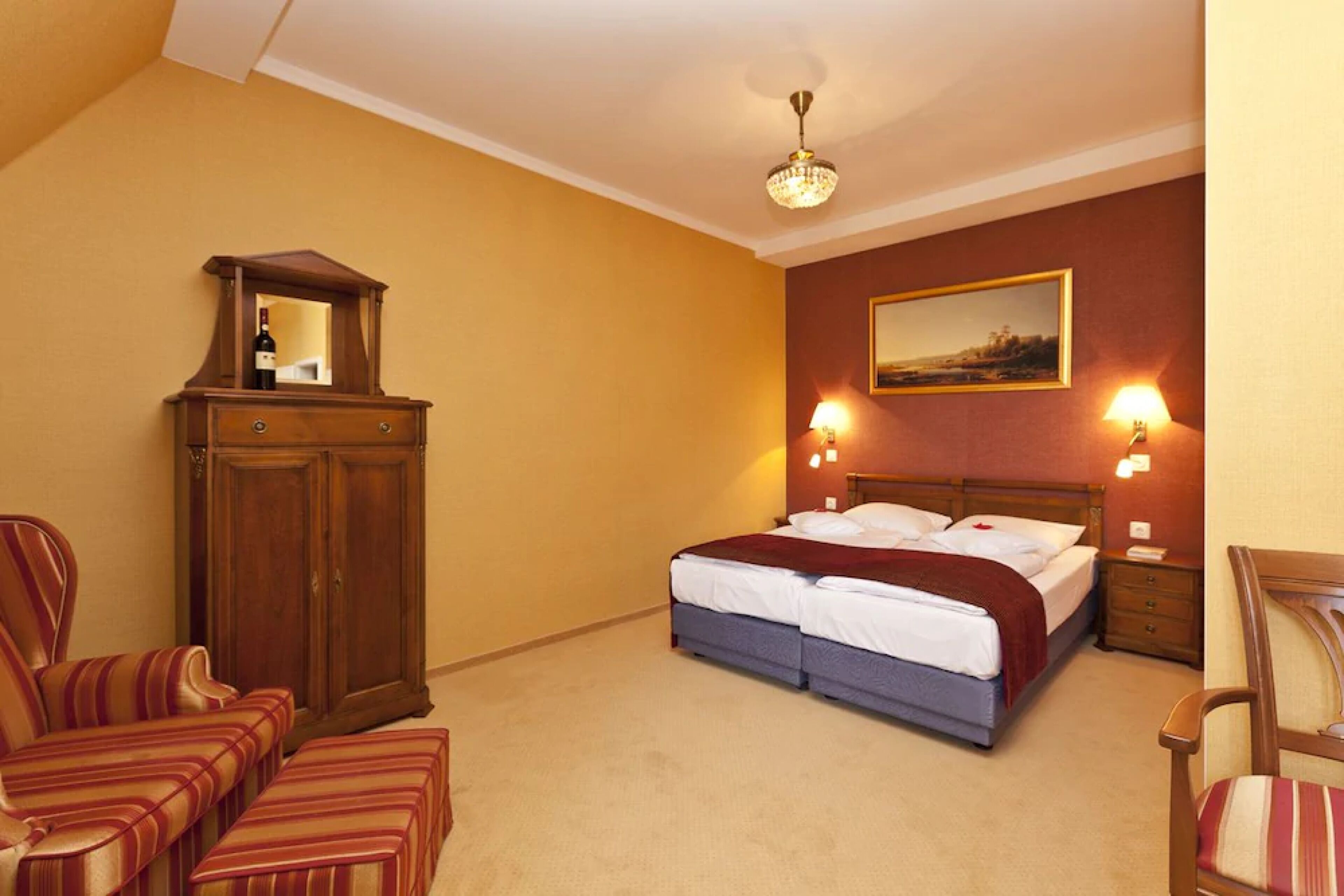 A bedroom with a double bed, a wooden wardrobe, two bedside lamps, and a chandelier.