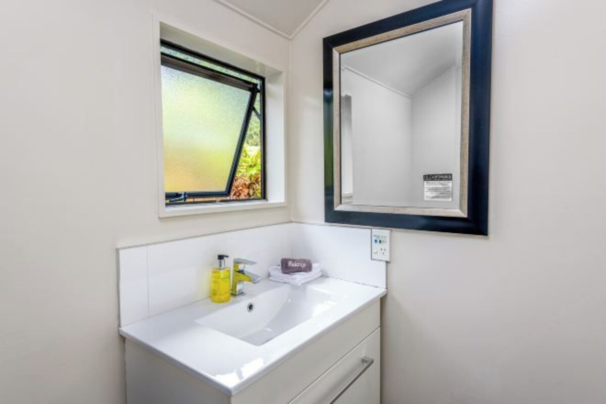 A bathroom with a white sink, a mirror, and a window with a view of greenery.