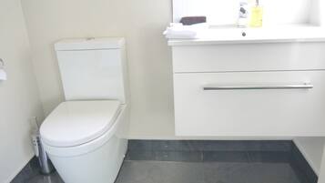 Un baño moderno con inodoro blanco, lavabo con espejo y dispensador de jabón.