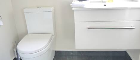 Un baño moderno con inodoro blanco, lavabo con espejo y dispensador de jabón.