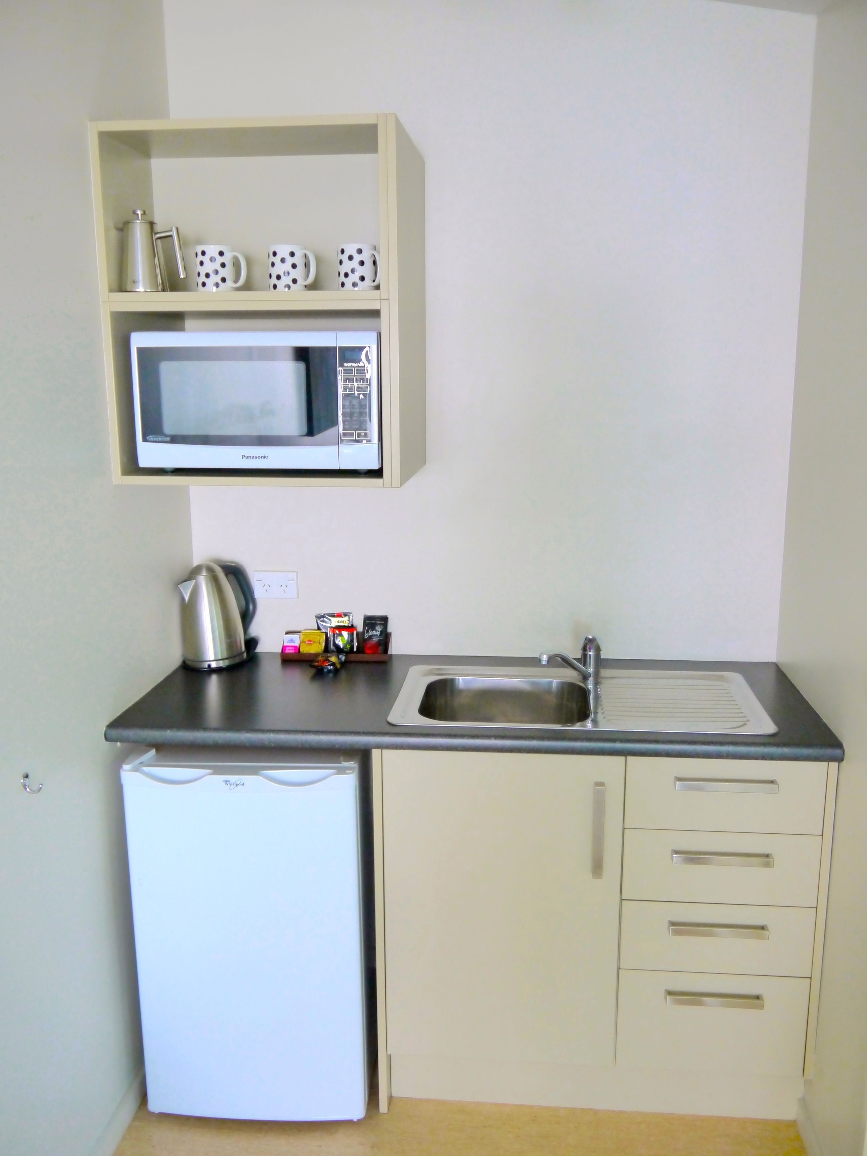 Una cocina compacta con microondas, hervidor y lavabo.