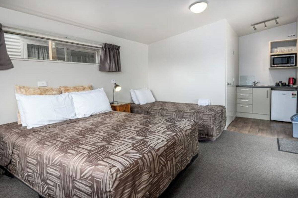 A hotel room with two beds, a kitchenette, and a window with curtains.