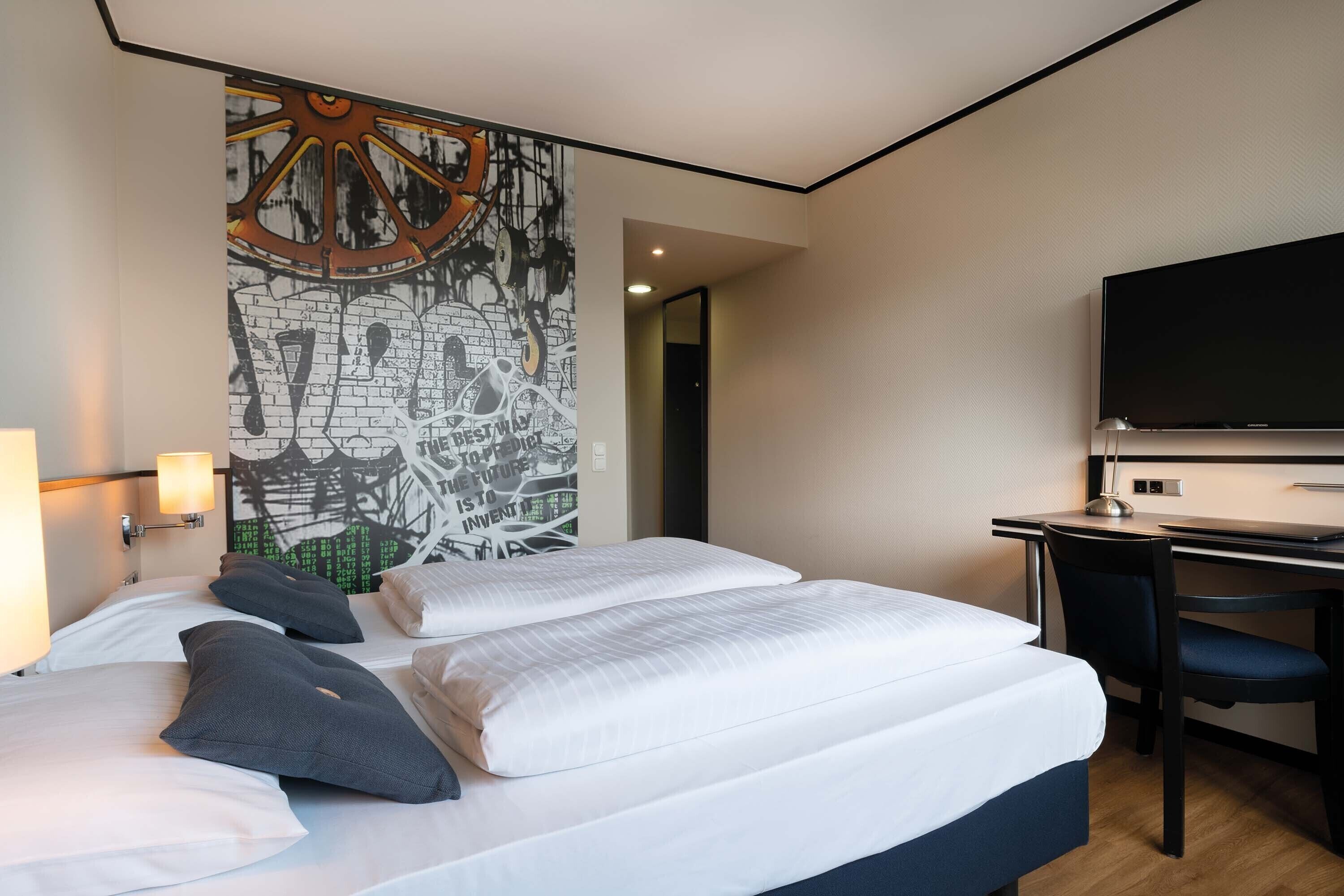 Een hotelkamer met twee bedden, een bureau, een stoel, een televisie en een muurschildering.