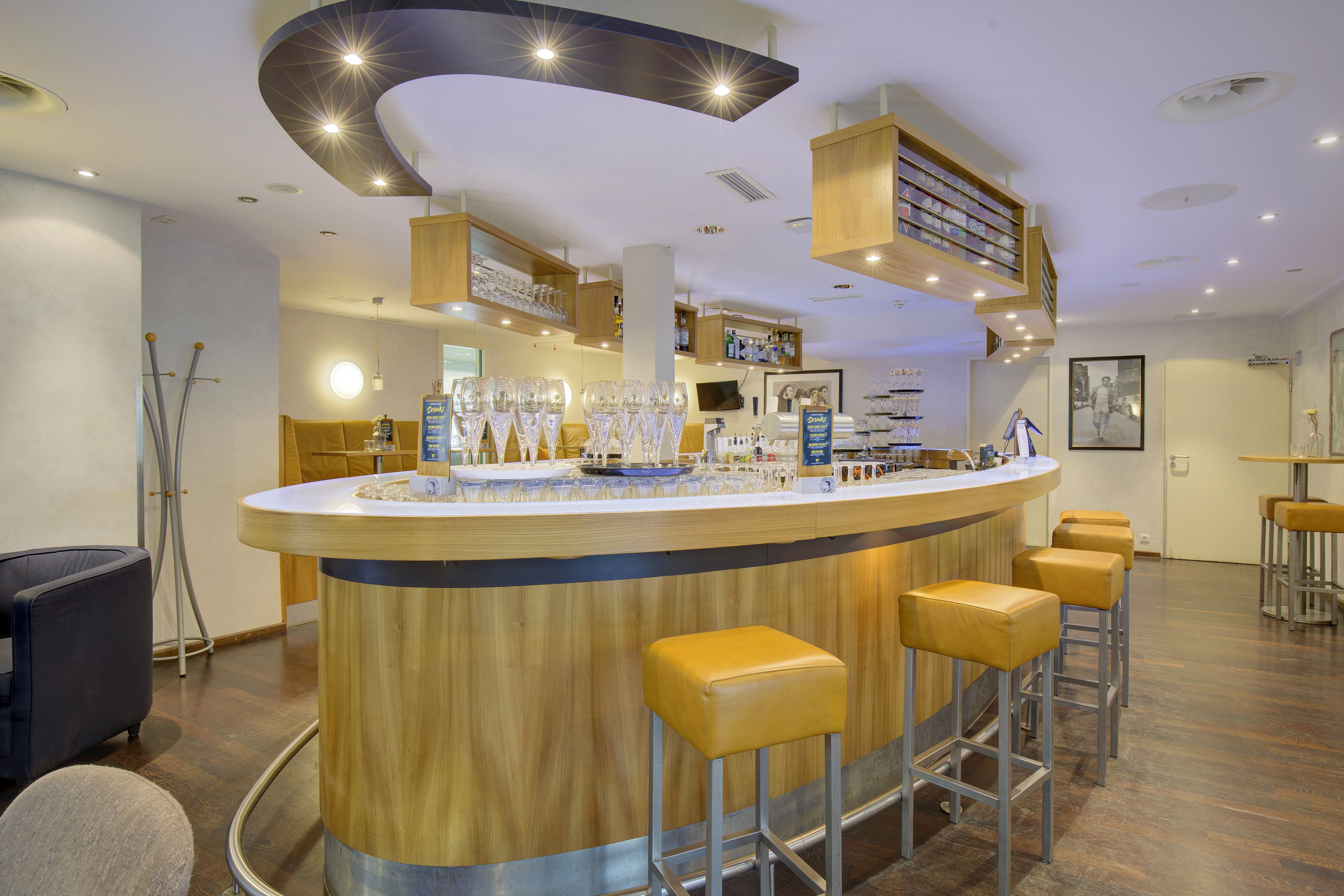 A bar area with a curved wooden counter, multiple stools, and a variety of glassware.