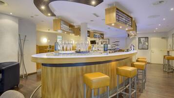 Un espace bar doté d’un comptoir en bois incurvé, de plusieurs tabourets et d’une variété de verres.