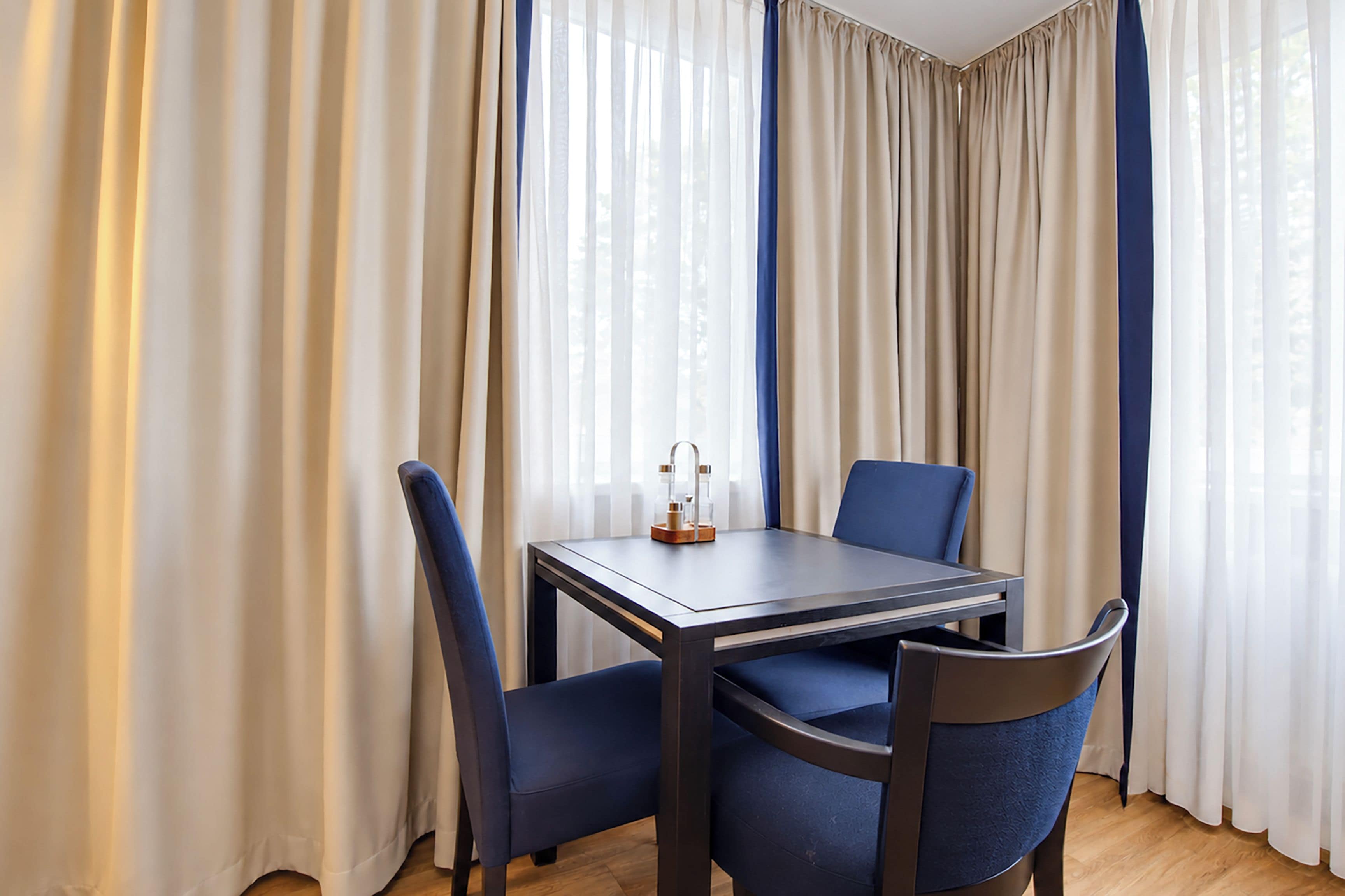 A room with a table and chairs, a window with curtains, and a wooden floor.