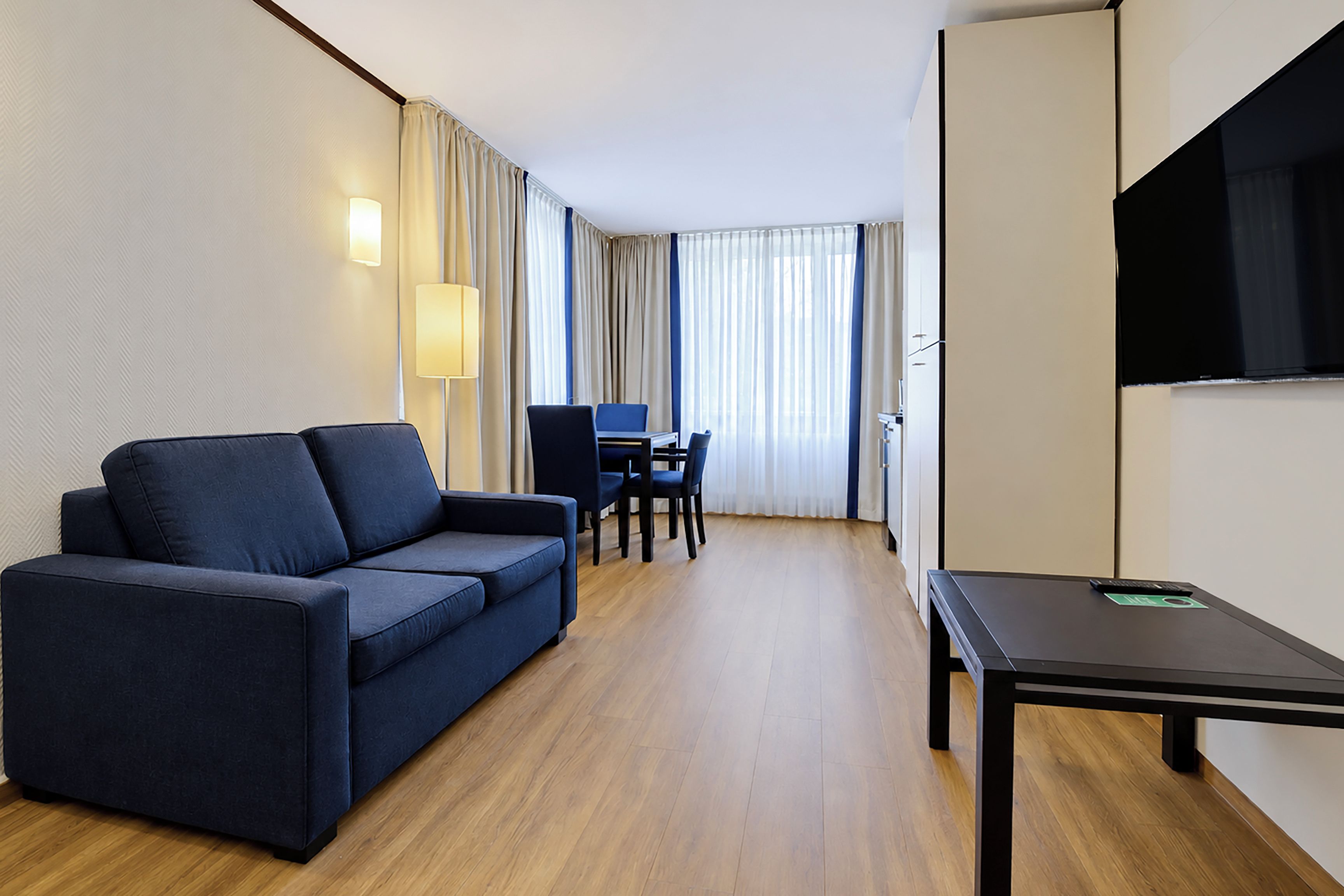 Habitación de hotel con sofá, escritorio, silla, televisión y ventana con cortinas.