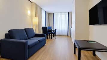 Habitación de hotel con sofá, escritorio, silla, televisión y ventana con cortinas.