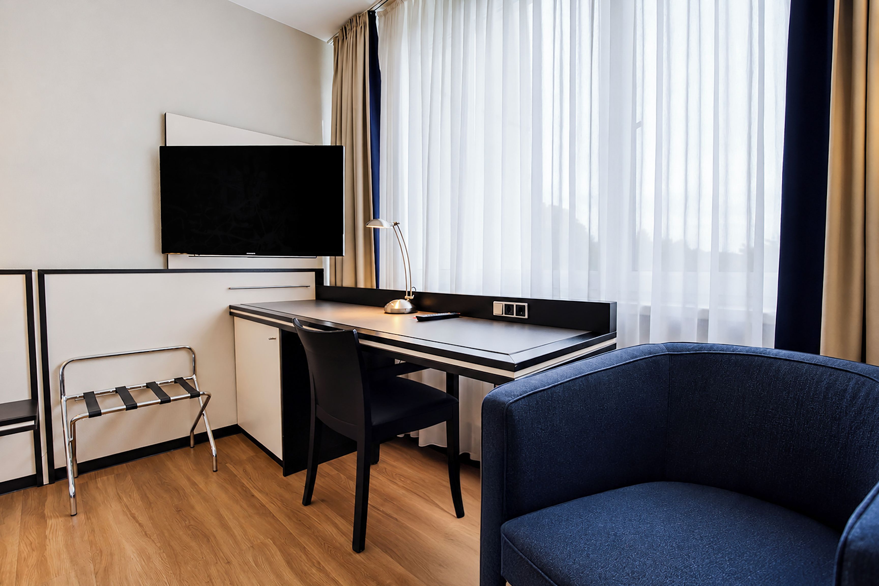 Een hotelkamer met een bureau, stoel, televisie en een raam met gordijnen.