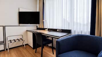 Een hotelkamer met een bureau, stoel, televisie en een raam met gordijnen.