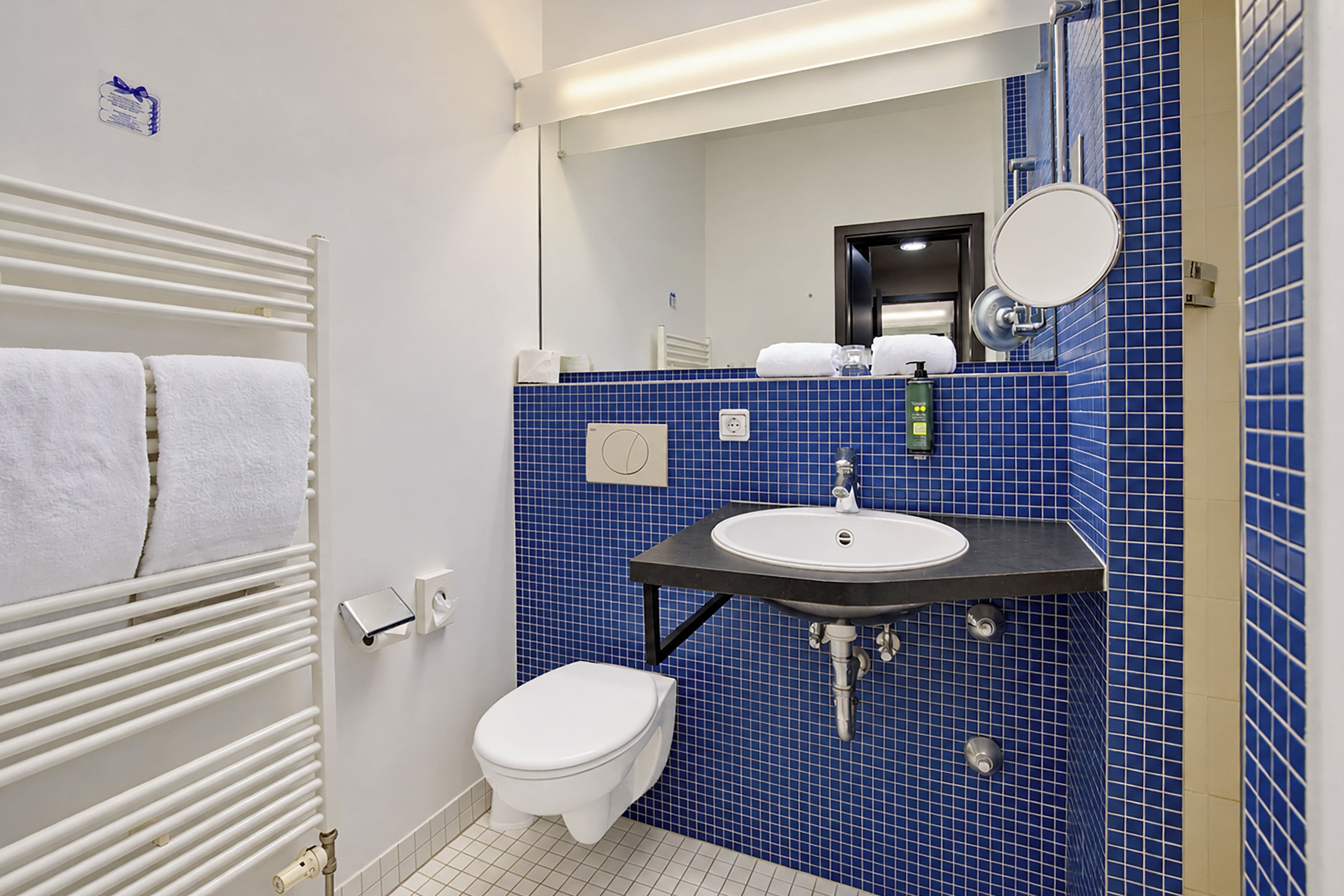 A bathroom with a white toilet, a sink with a mirror above it, and a towel rack with white towels.