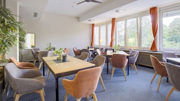 Een vergaderzaal met een lange tafel, meerdere stoelen, een plafondventilator en grote ramen met gordijnen.