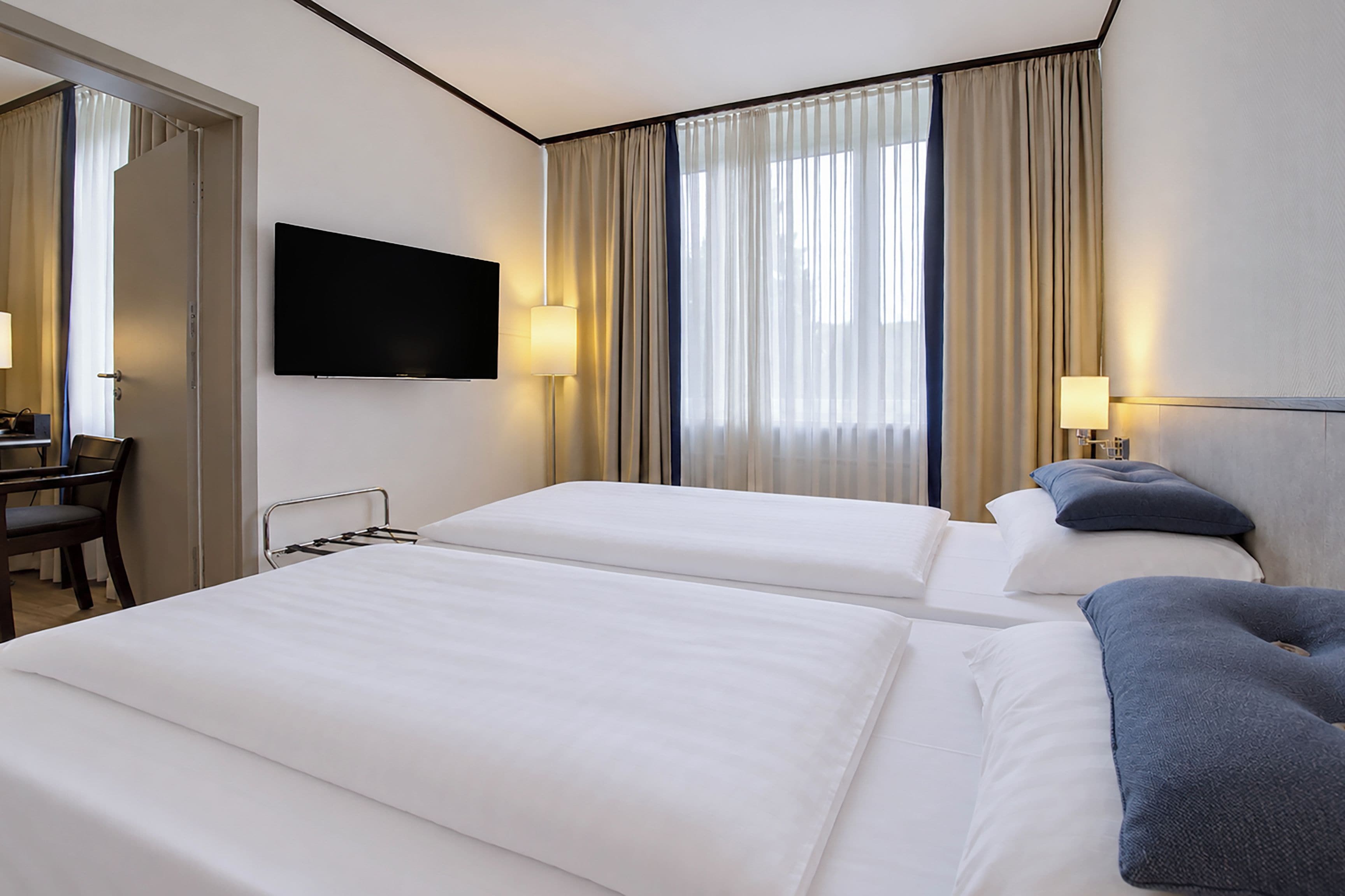 Una habitación de hotel con dos camas, un televisor montado en la pared y un escritorio con una silla.