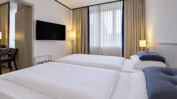 Una habitación de hotel con dos camas, un televisor montado en la pared y un escritorio con una silla.