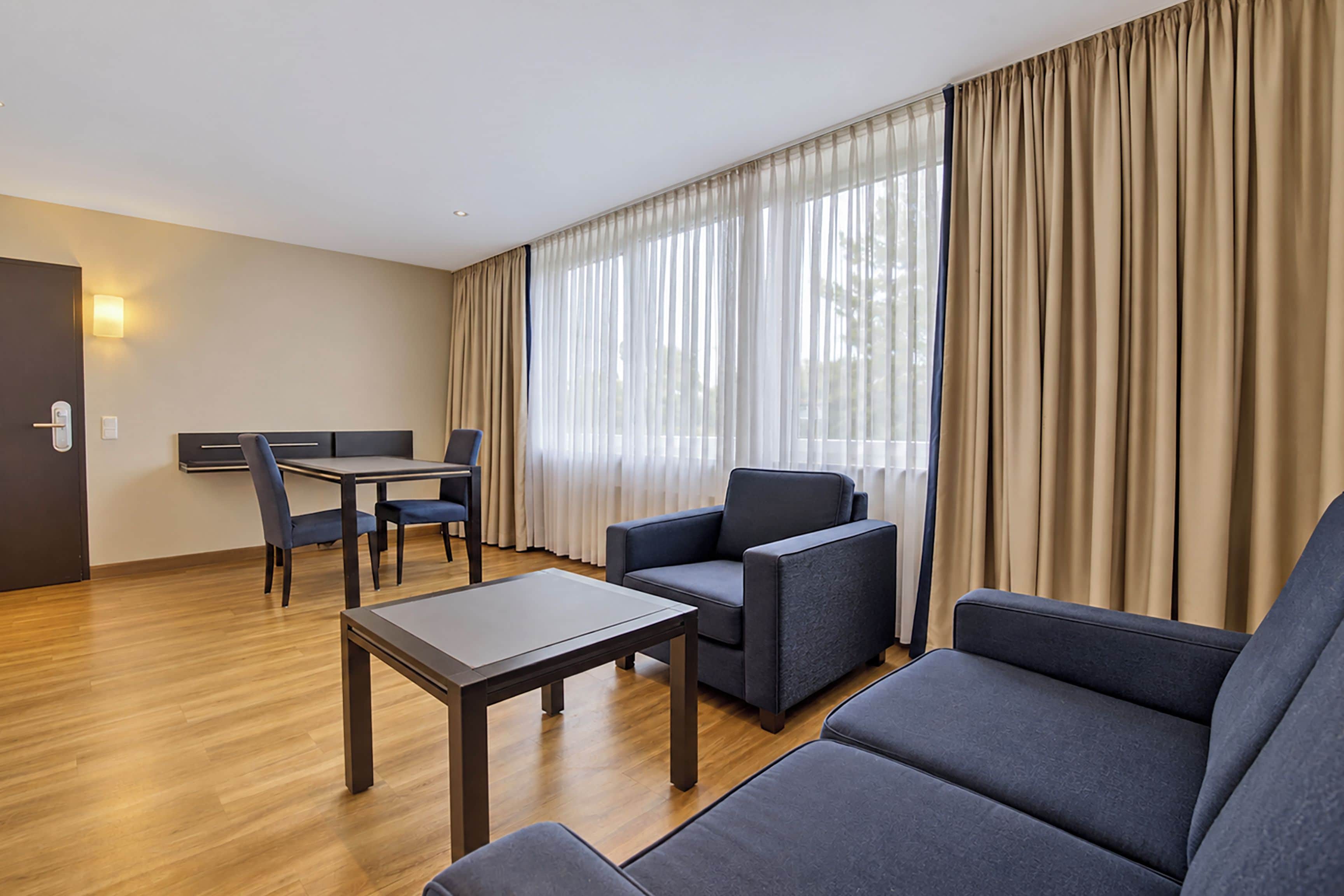 Een hotelkamer met een bank, fauteuil, eettafel en stoelen.