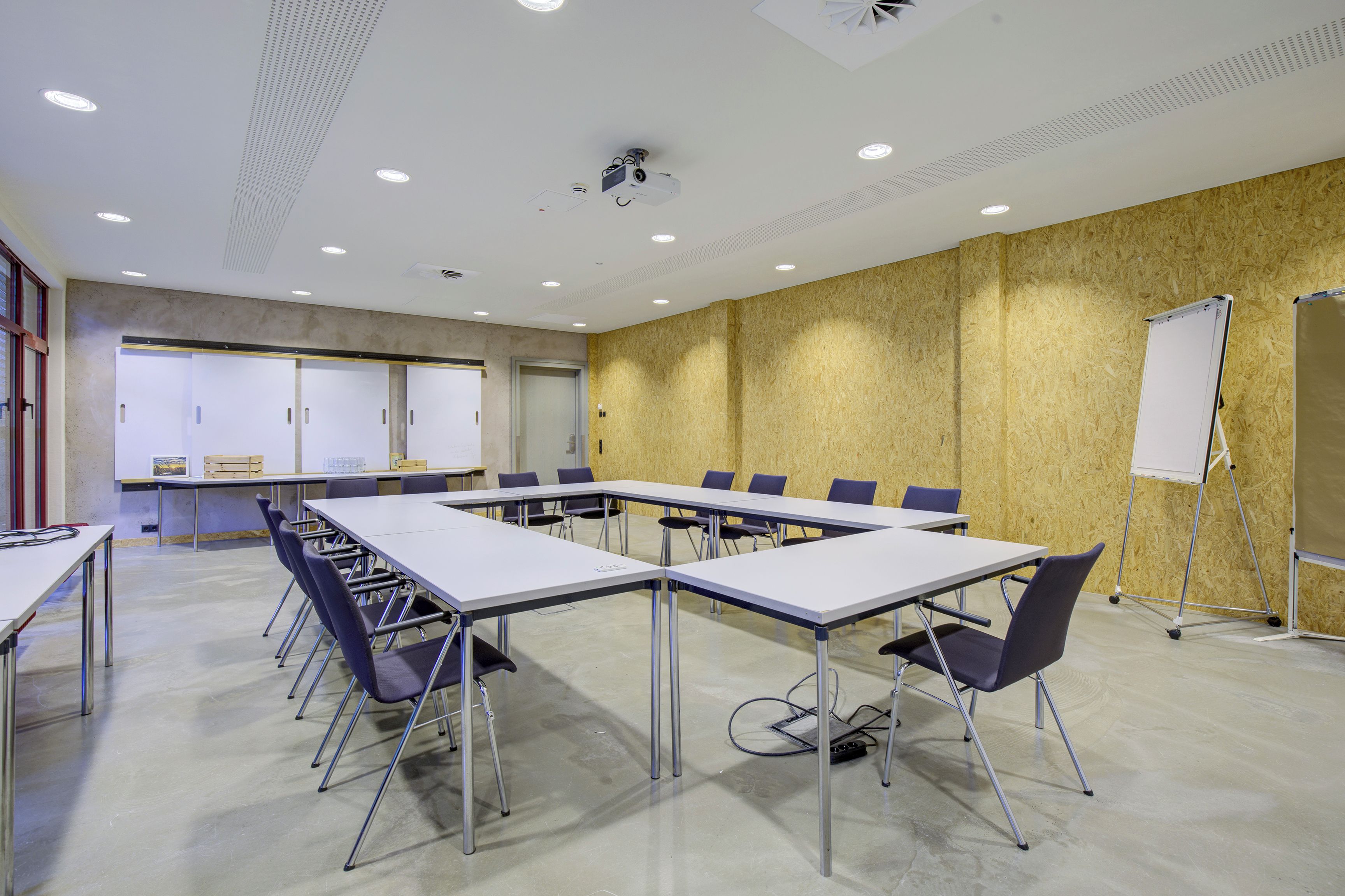 Un salón de conferencias con una larga mesa, sillas, una pizarra y un proyector.