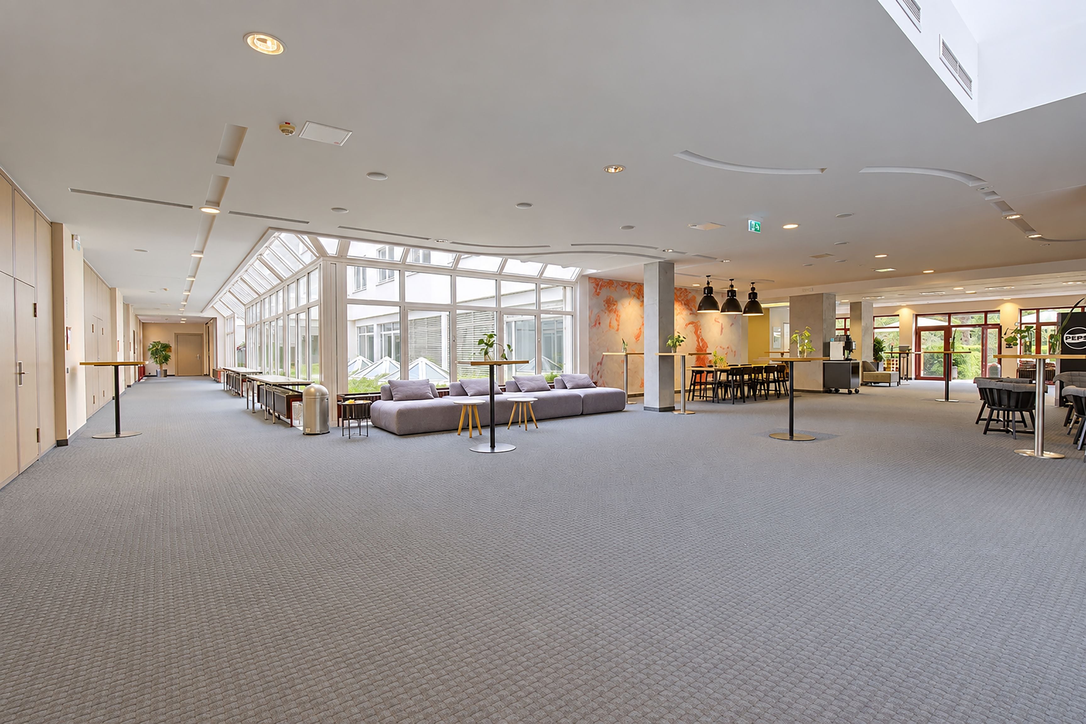 Eine geräumige Hotelhalle mit hoher Decke, großen Fenstern, einer Sitzecke mit Sofas und einer Bar.